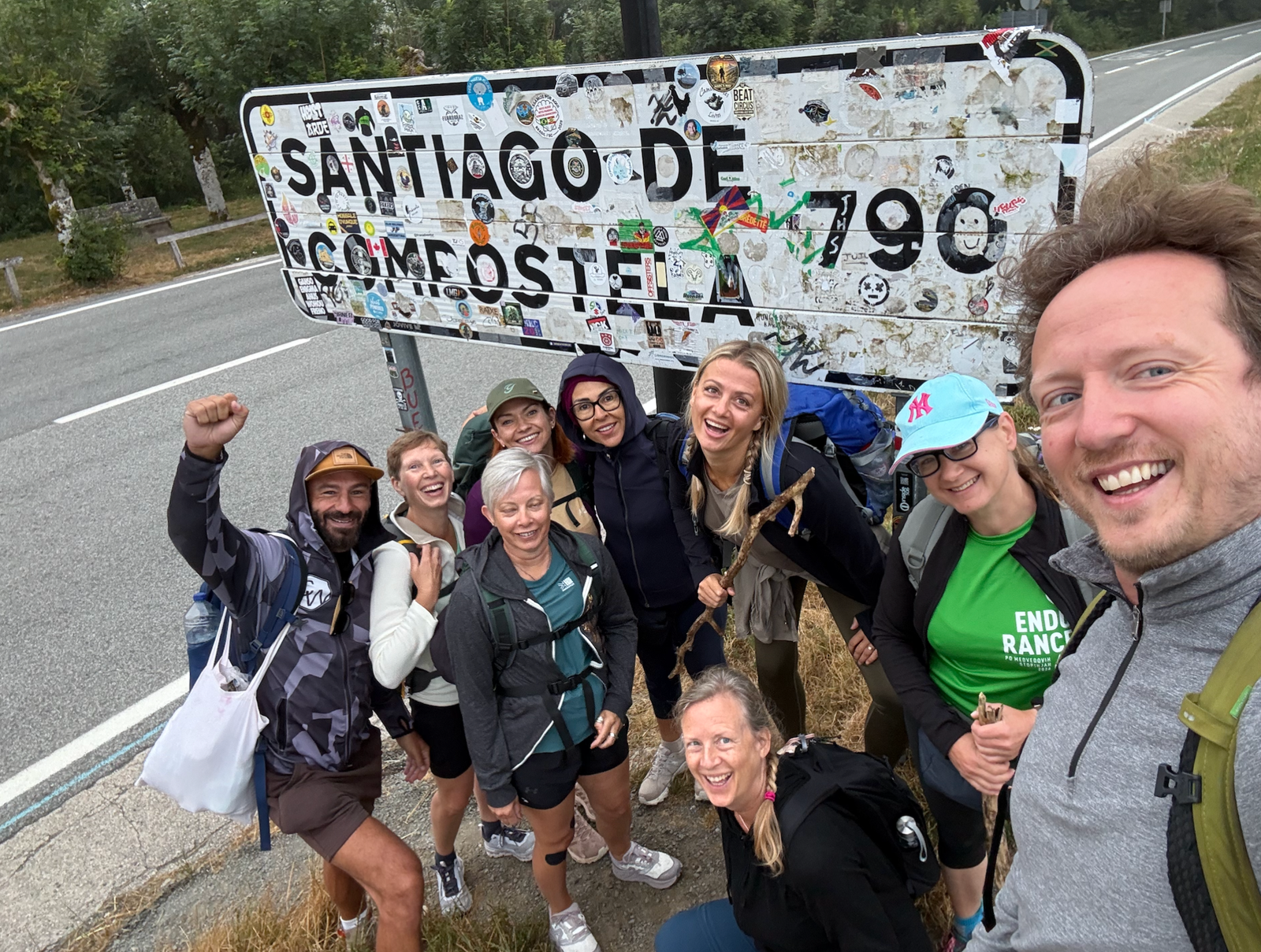 Peter and fellow pilgrims smiling beside a Santiago de Compostela distance marker